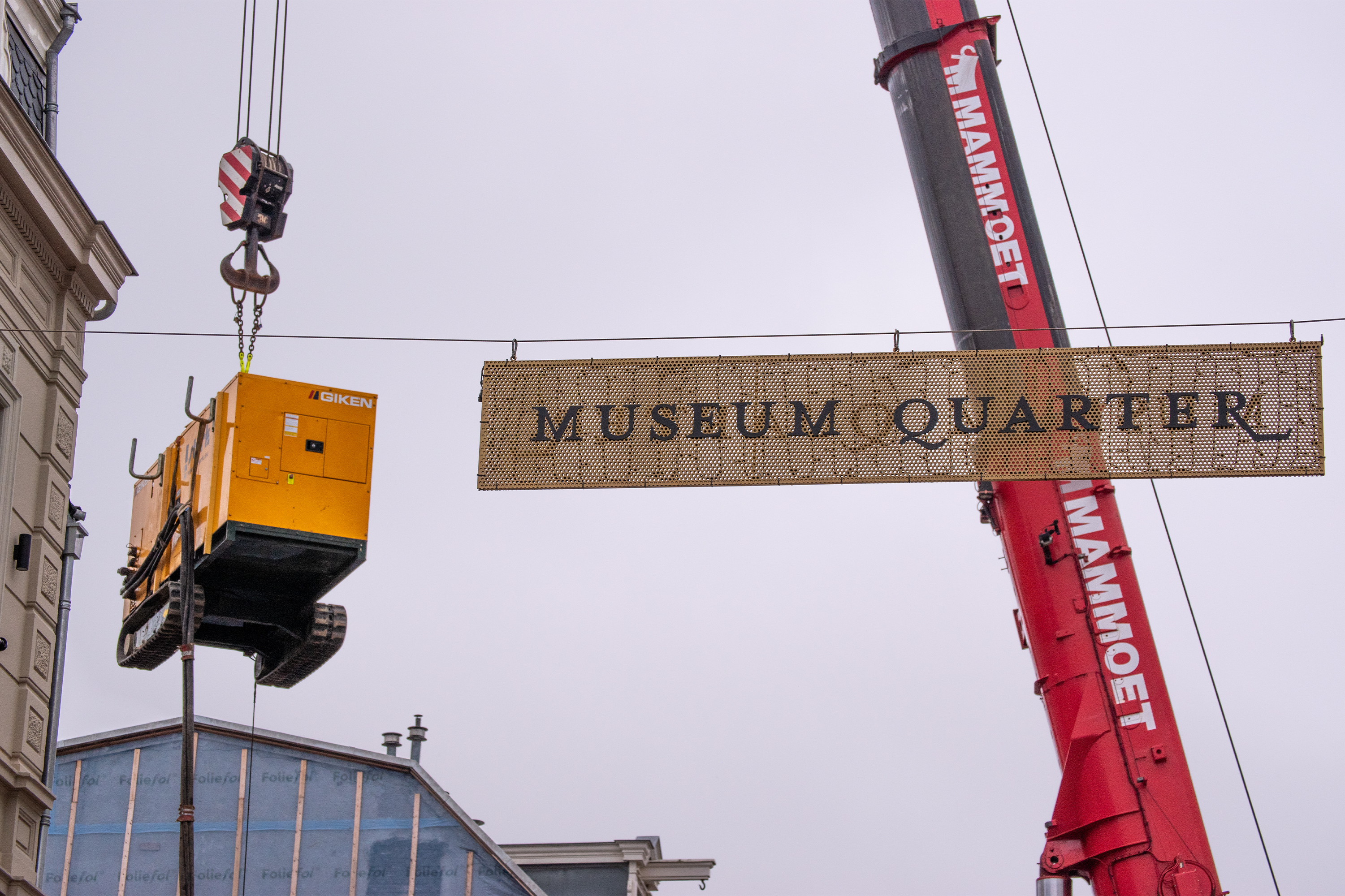 image of heavy vehicle on tracks, suspended by crane alongside signage saying 'Museum Quarter'